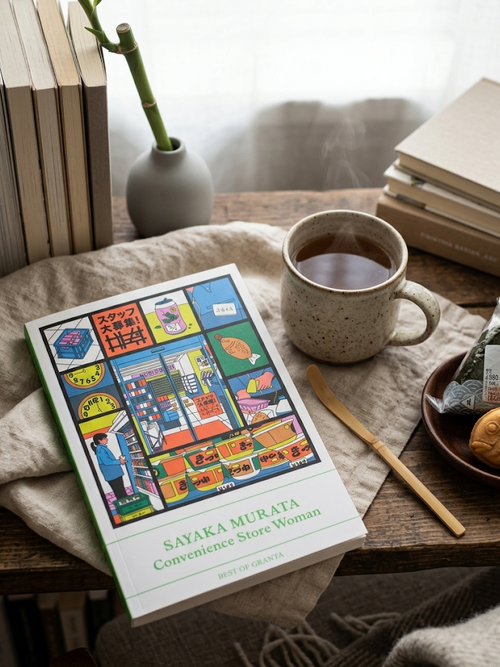 Book titled 'Convenience Store Woman' by Sayaka Murata on a wooden table with a cup of coffee and snacks.