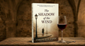 Book titled 'The Shadow of the Wind' by Carlos Ruiz Zafon with a glass of red wine and key on a wooden surface.